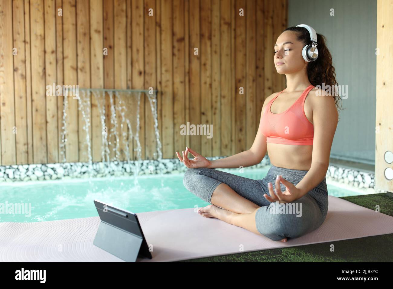 Woman e-learning yoga using laptop and headphones to meditate in a spa Stock Photo