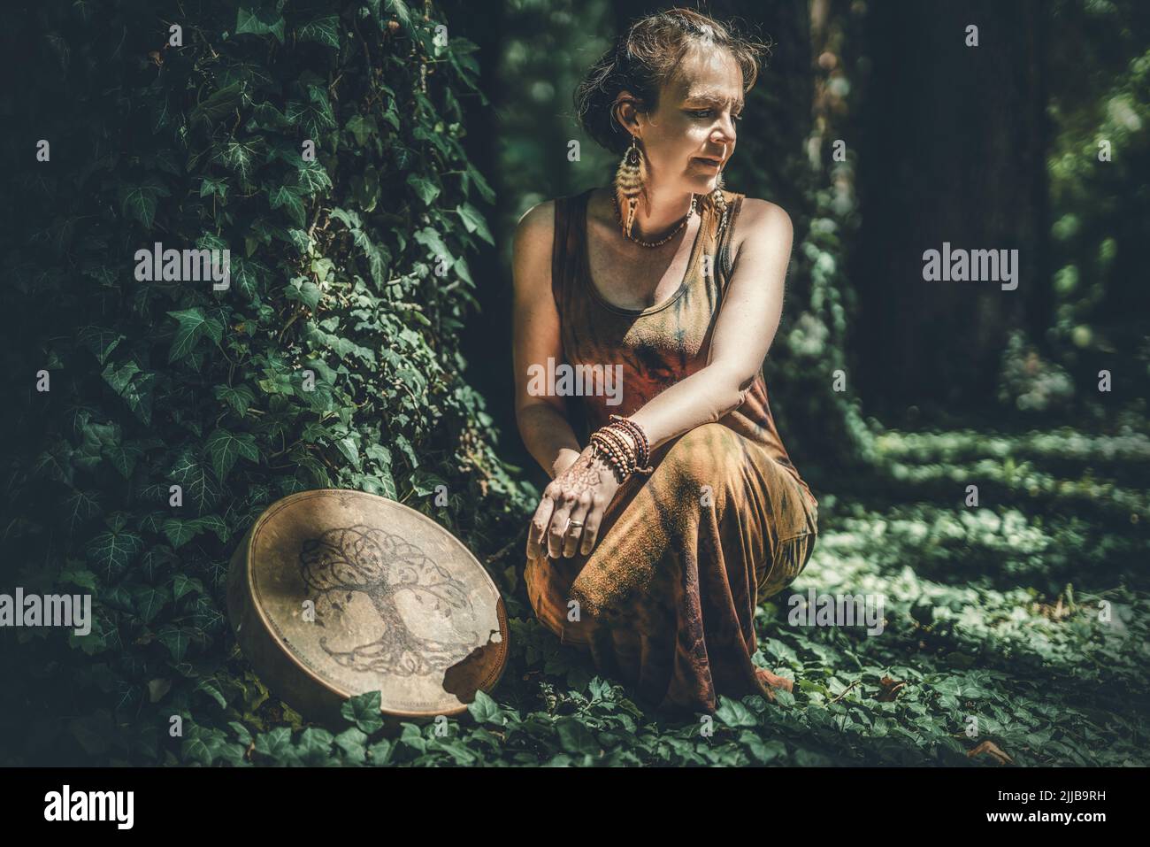 beautiful shamanic girl playing on shaman frame drum in the nature. Stock Photo