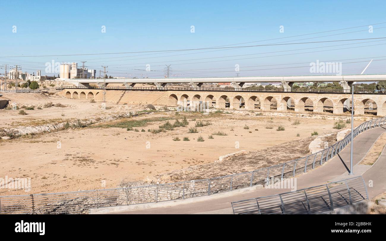 a modern train bridge spans the Beer Sheva River in front of the ancient Ottoman era train bridge with a modern bike path in the foreground Stock Photo