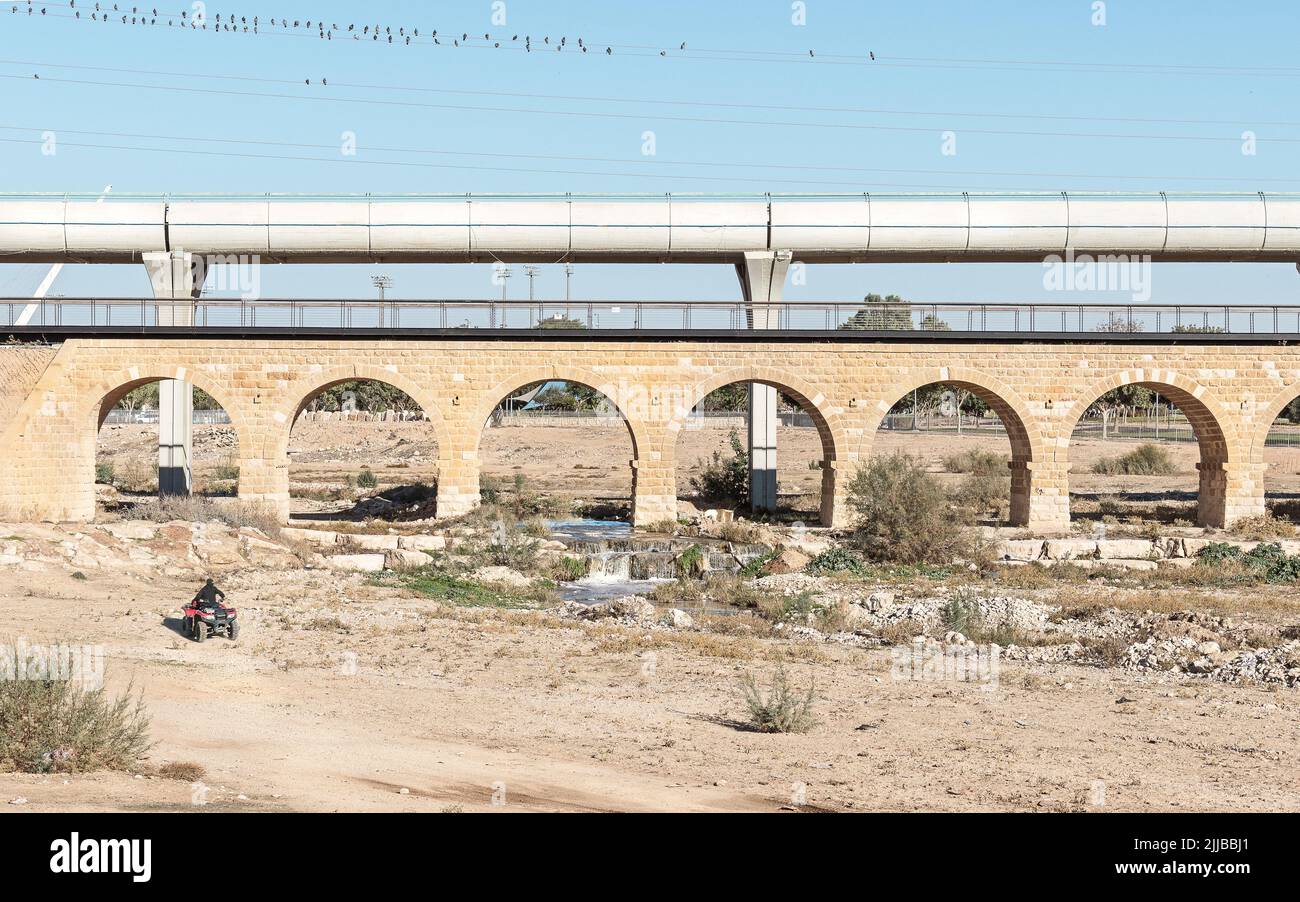 reconstructed limestone Ottoman era train bridge in front of a modern train bridge over the Beer Sheva River in Israel with a clear blue sky and an AT Stock Photo