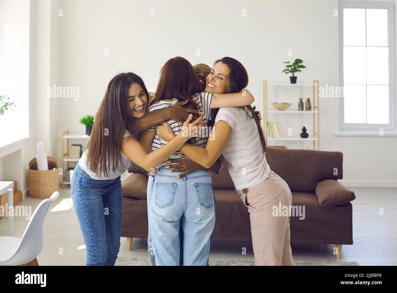 Group of happy young women hugging their friend and congratulating her on success Stock Photo
