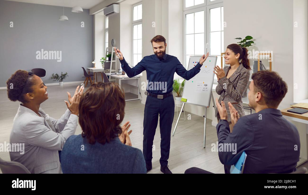 Cheerful colleagues applauding man after successful presentation in office on whiteboard. Stock Photo