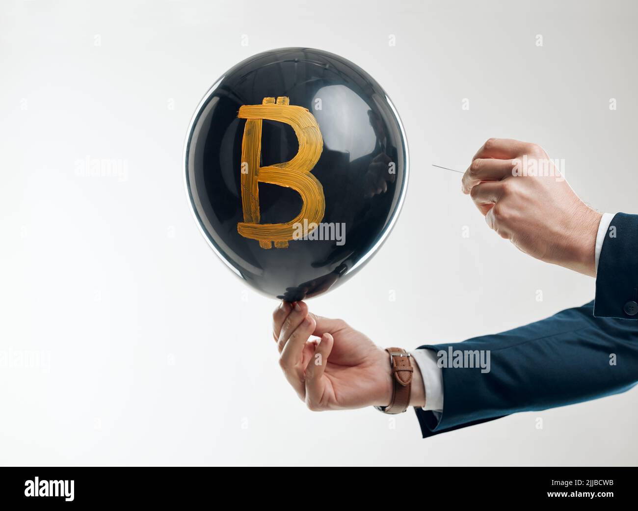 Appreciation and depreciation takes place within seconds. Studio shot of an unrecognisable businessman holding a pin to pop a balloon with a bitcoin Stock Photo