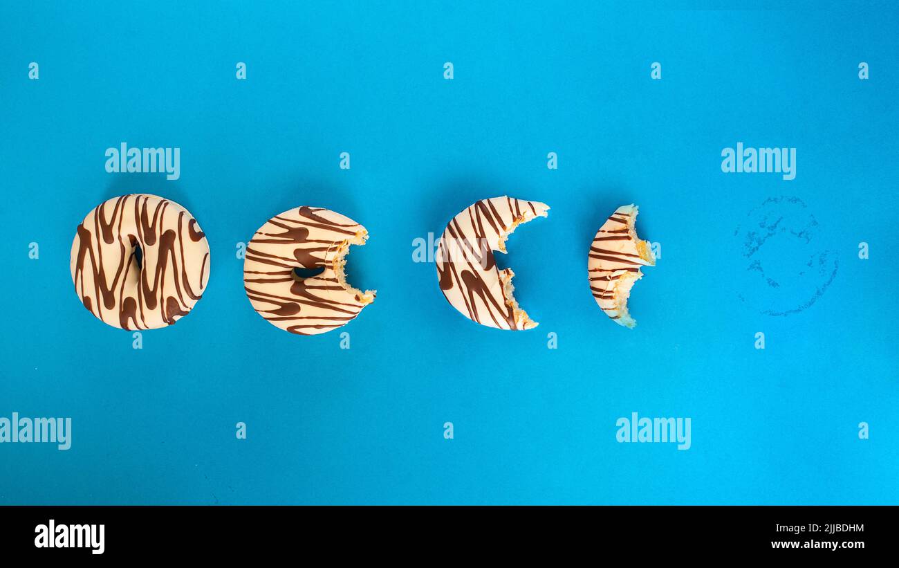 Eaten donut  with white chocolate and dark stripe on blue background. Top view. Stock Photo