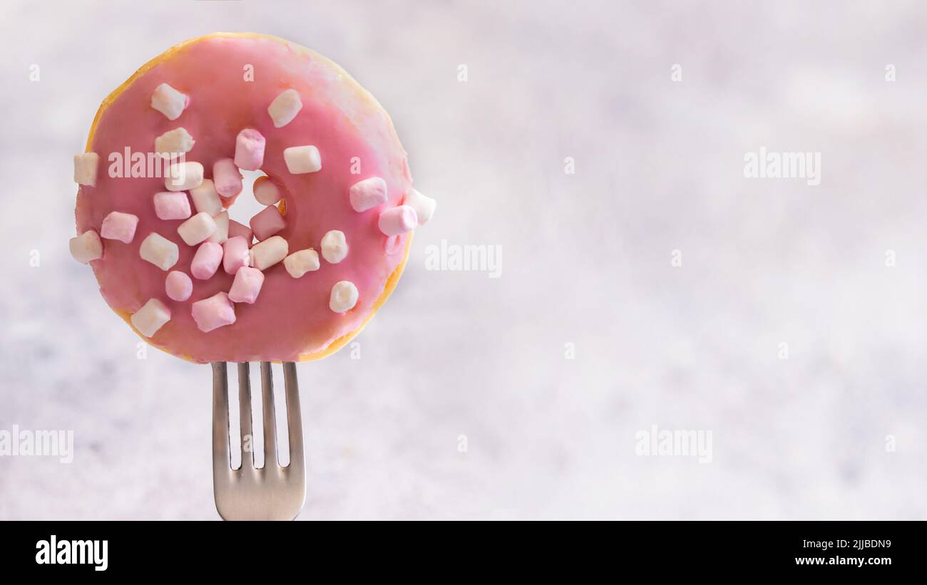 Close up of fork with  pink glazed donut with marshmallow .Large doughnut background with copy space for banner Stock Photo