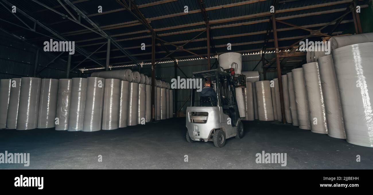 Forklift transports large roll of paper at recycling and toilet paper manufacturing plant. Stock Photo