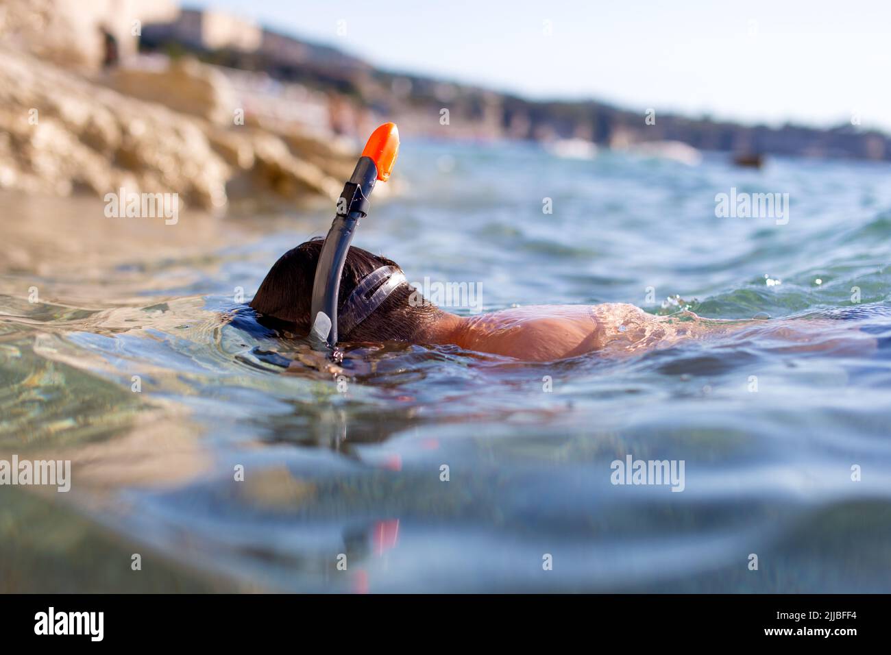 Boy in goggles and pipe diving in sea at rocky shore during summer Stock Photo