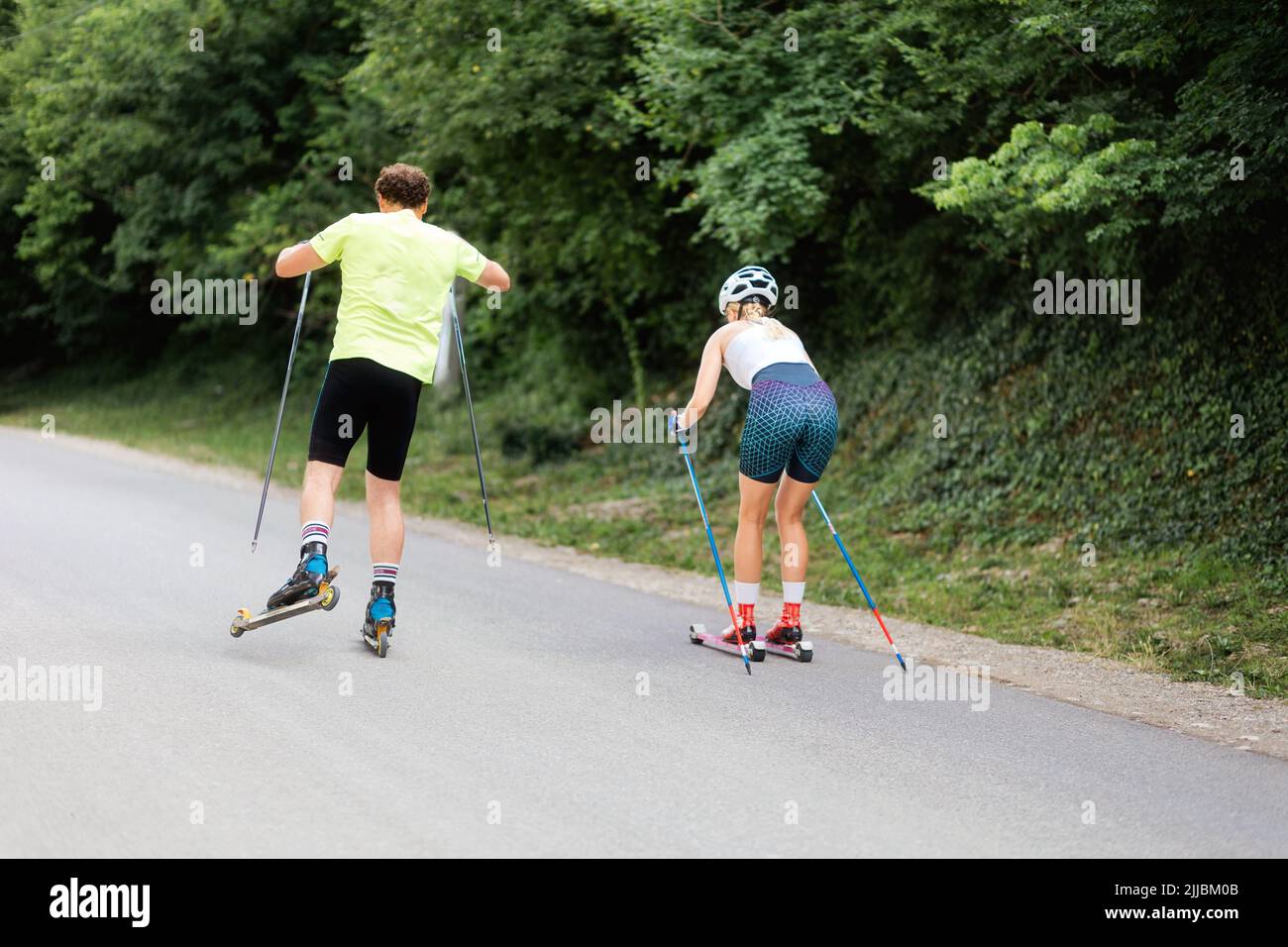 Athletic woman and man together training on the roller ski. Back view. Concept of competition, biathlon, and summer workout. Stock Photo