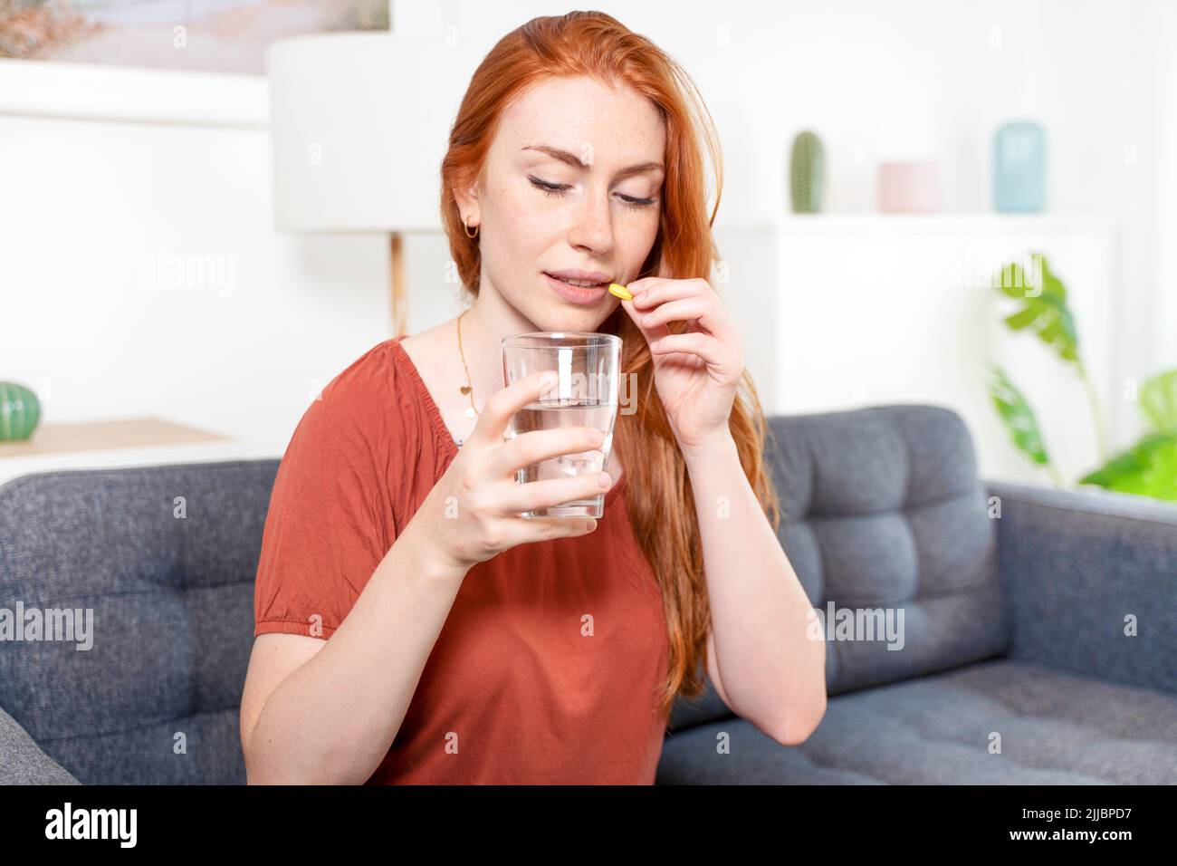 Woman taking vitamins while sitting on the couch at home Stock Photo