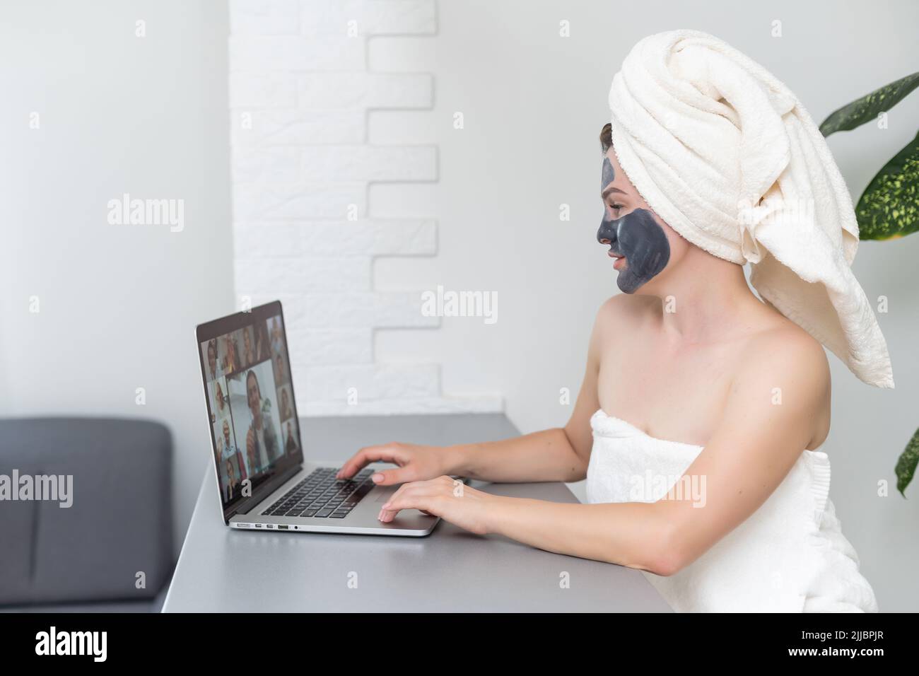 Young woman with towel on head and black facial clay mask sitting at ...