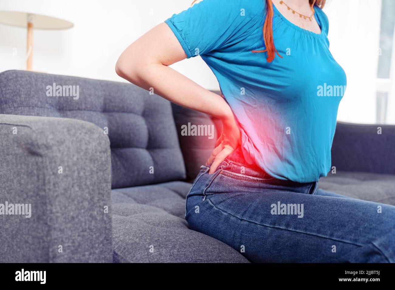 Woman low back close up suffering back pain sitting on the couch at home Stock Photo