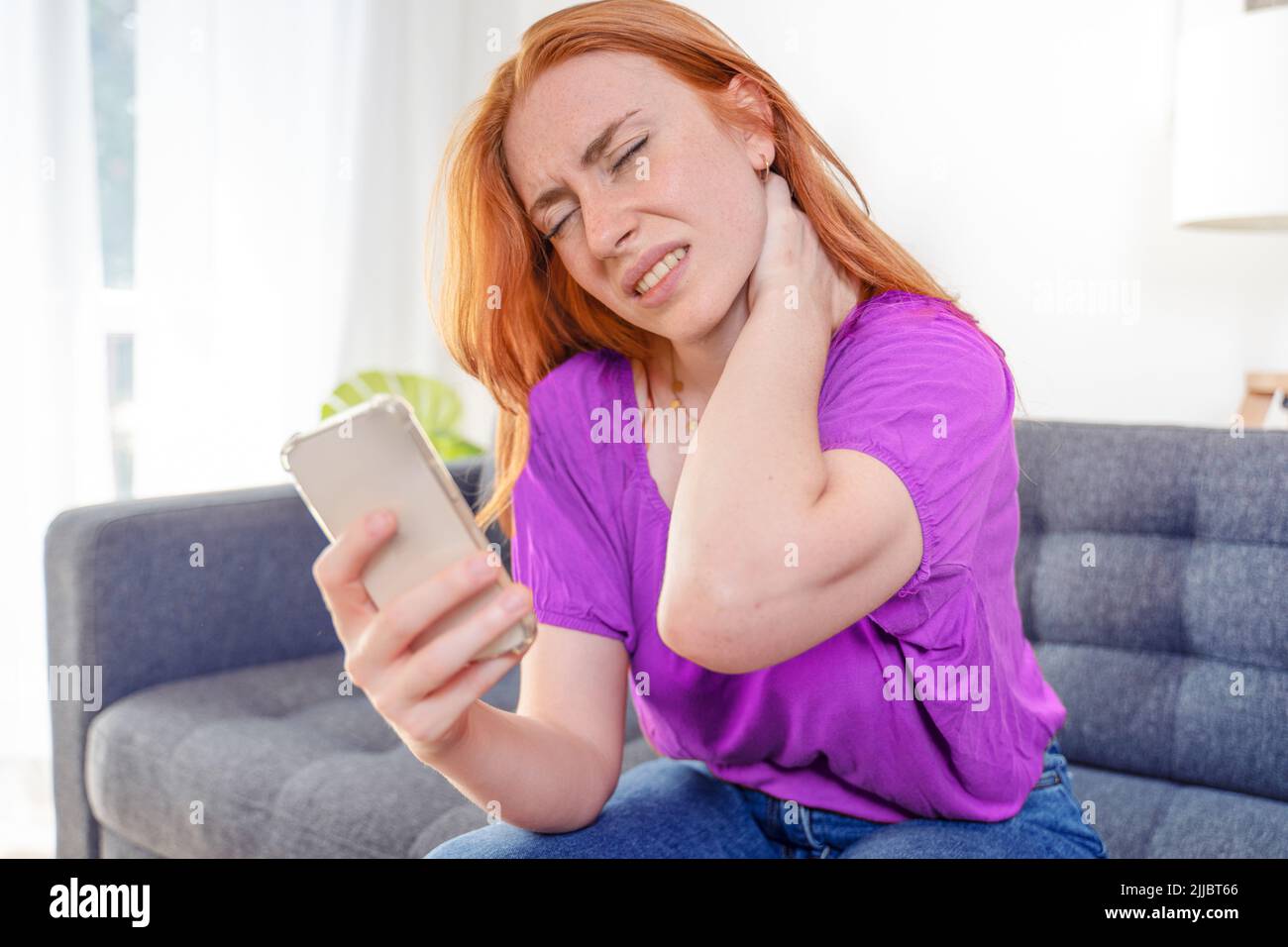 Woman suffering pain in head and neck watching mobile phone Stock Photo