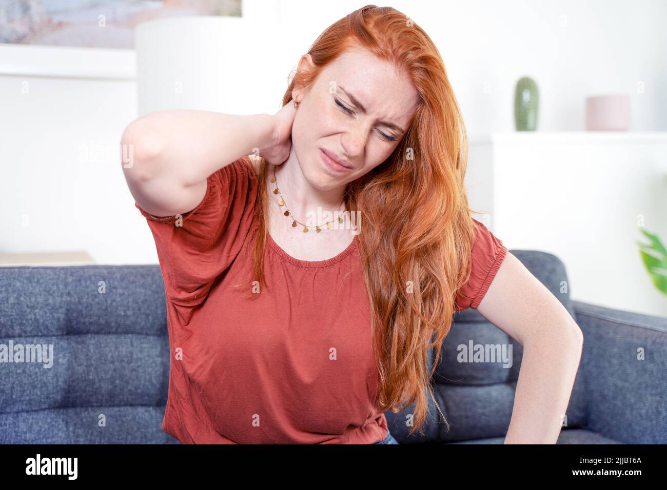 Woman sitting on couch and suffers from neck pain Stock Photo