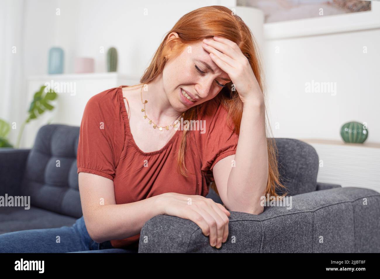 Girl sits on the sofa suffer chronic head pain Stock Photo