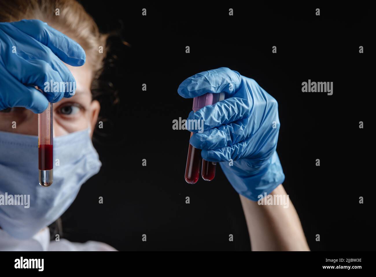 A female virologist works with blood tubes against a black background ...