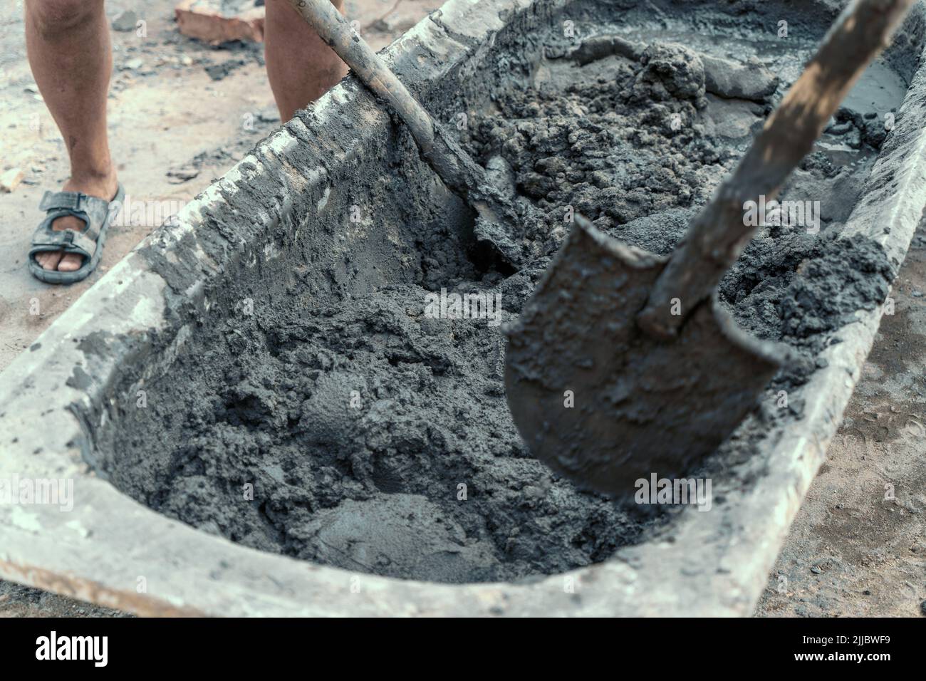 Workers stir or mix cement with shovels at construction site. Stock Photo