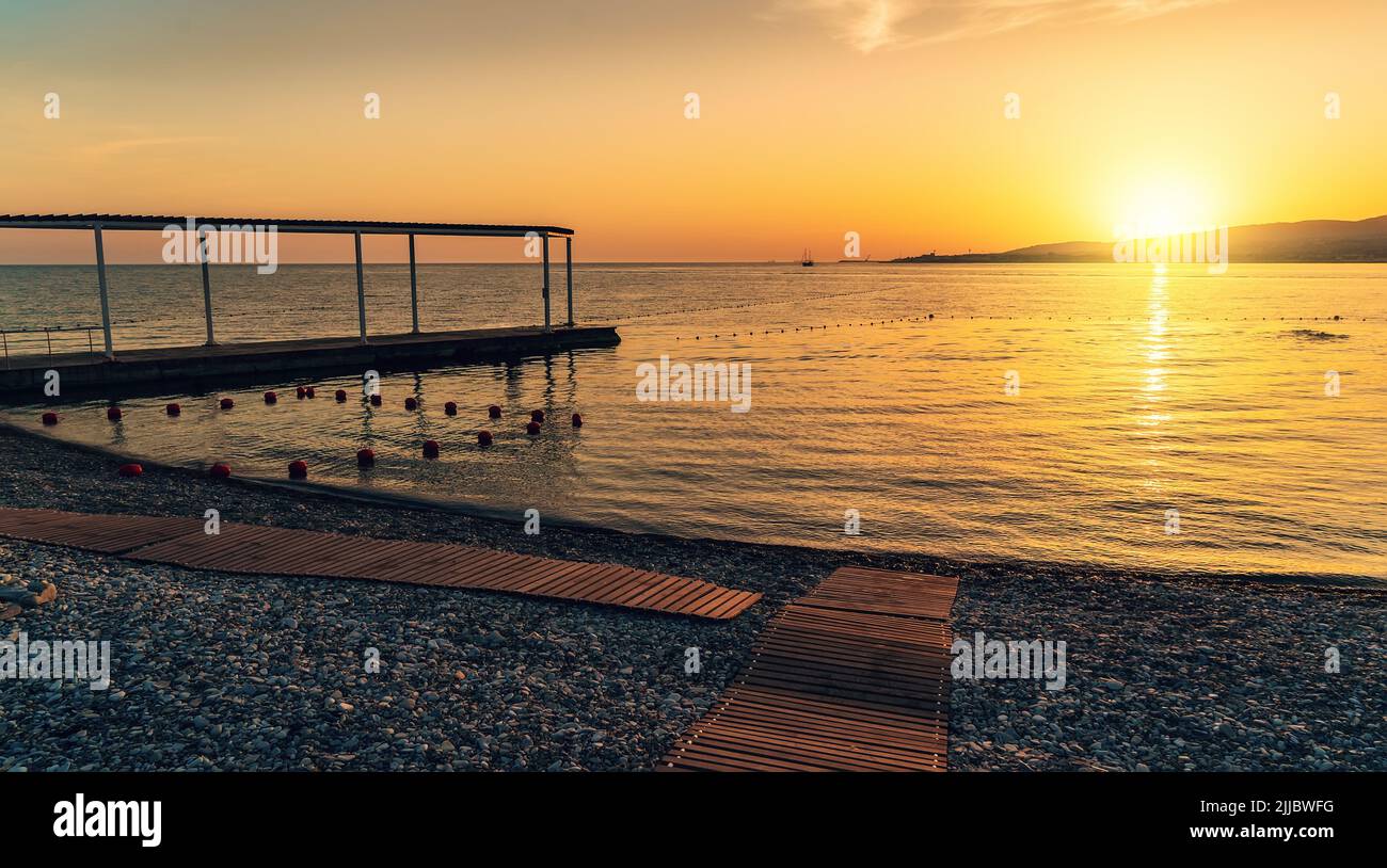Sunset with yellow sun above sea surface and stone beach. Stock Photo