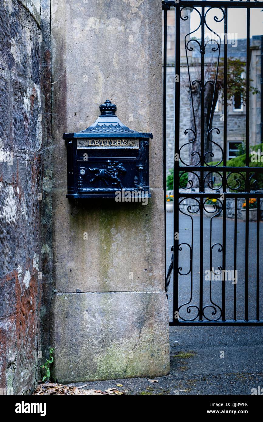 Portrait view, exterior wall mounted black letterbox, embossed with the word letters and a postman riding a horse next to a gate Stock Photo