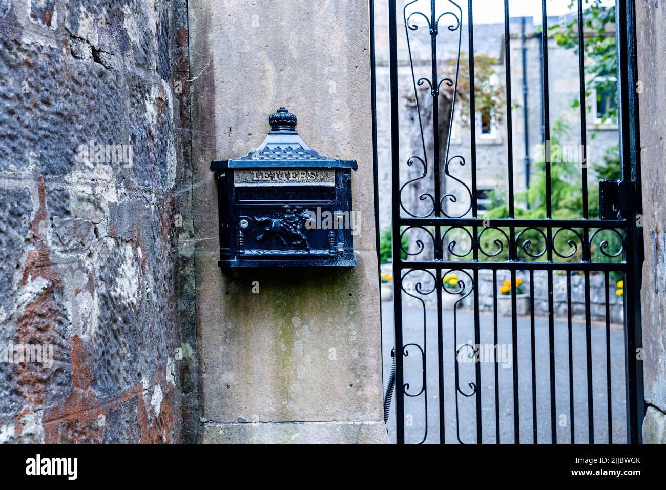 Landscape view, exterior wall mounted black letterbox, embossed with the word letters and a postman riding a horse next to a gate Stock Photo