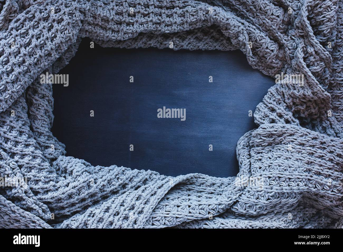 Grey woven blanket crumpled and framed over a dark toned black wooden background. Shot from above top view with free space for text for background. Stock Photo