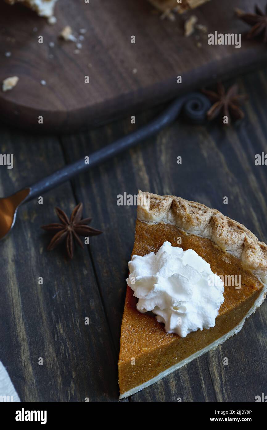 A slice of fresh baked pumpkin pie over wood background. Extreme selective focus on whipped cream with blurred foreground and background. Stock Photo