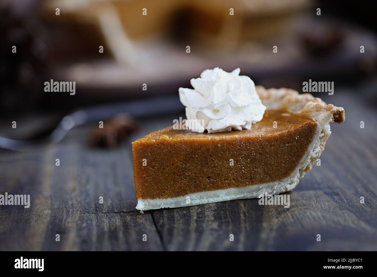 A slice of fresh baked pumpkin pie with whipped cream over wood background table. Extreme selective focus on whipped cream with blurred foreground and Stock Photo