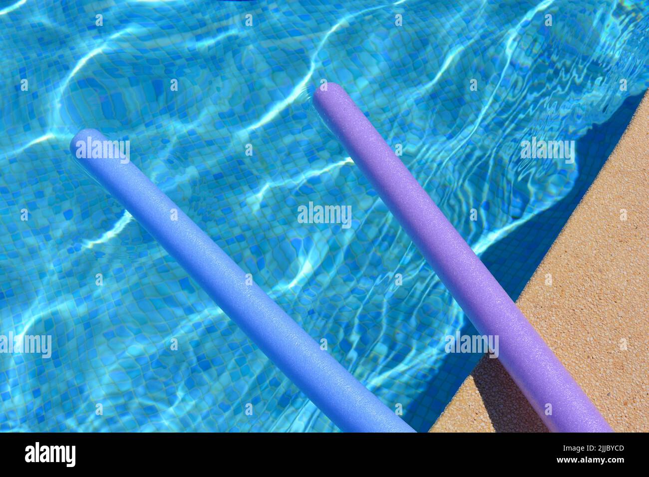 Summer vibes. Purple and blue swim noodles floating  at side of swimming pool Stock Photo