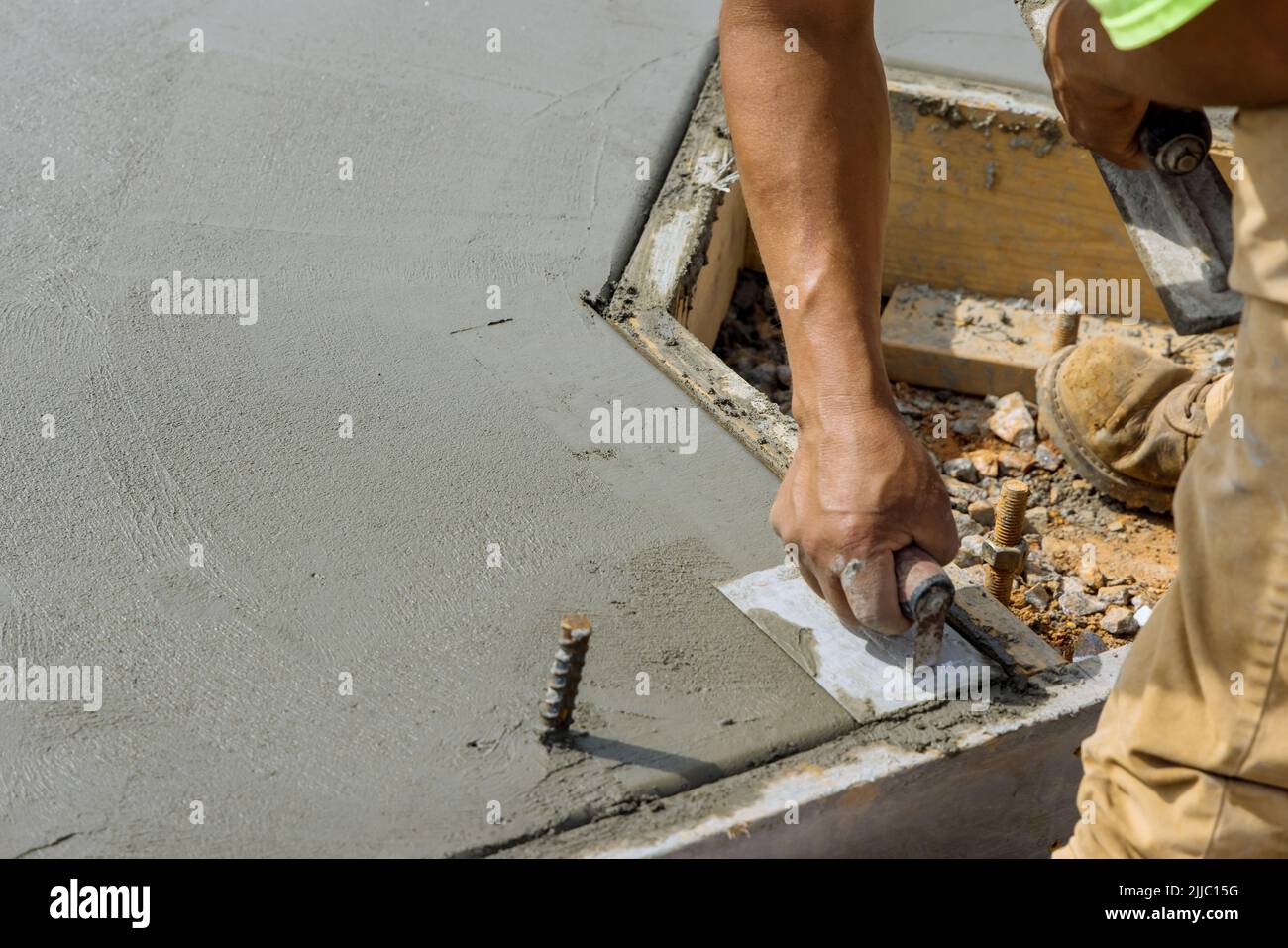 A masonry worker holds a steel trowel and is smoothing a cement floor