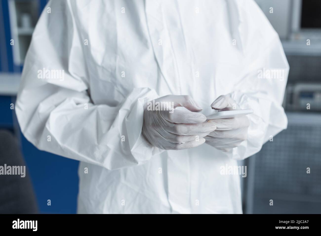 Cropped view of scientist in protective suit and latex gloves using mobile phone in lab Stock Photo