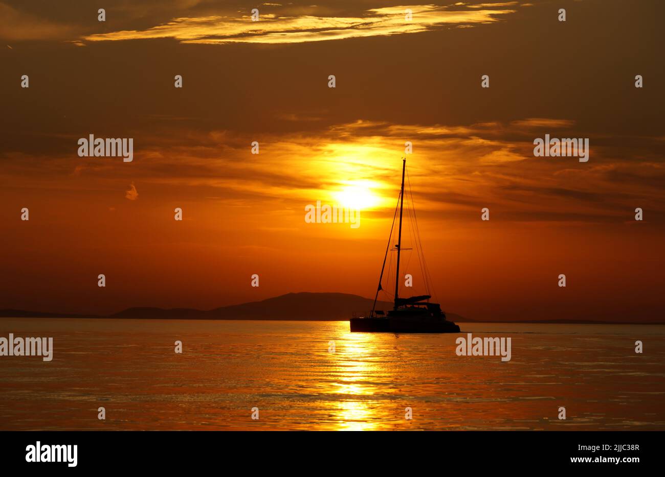 Black silhouette of yacht during summertime golden hour at scenic intensive color seascape Stock Photo