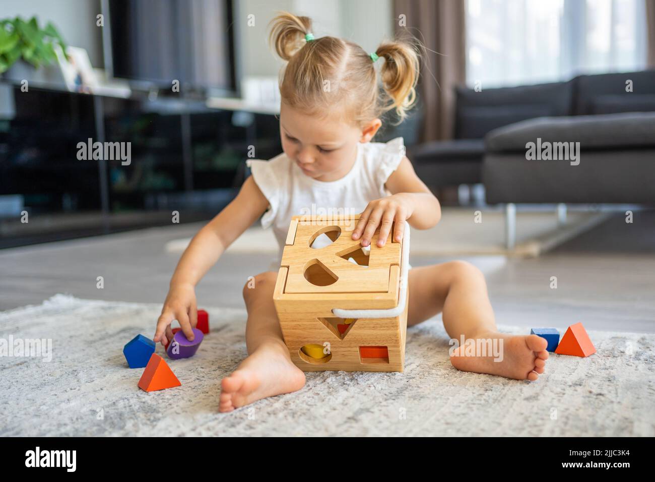 Cute caucasian little girl playing on the floor at home with eco wooden