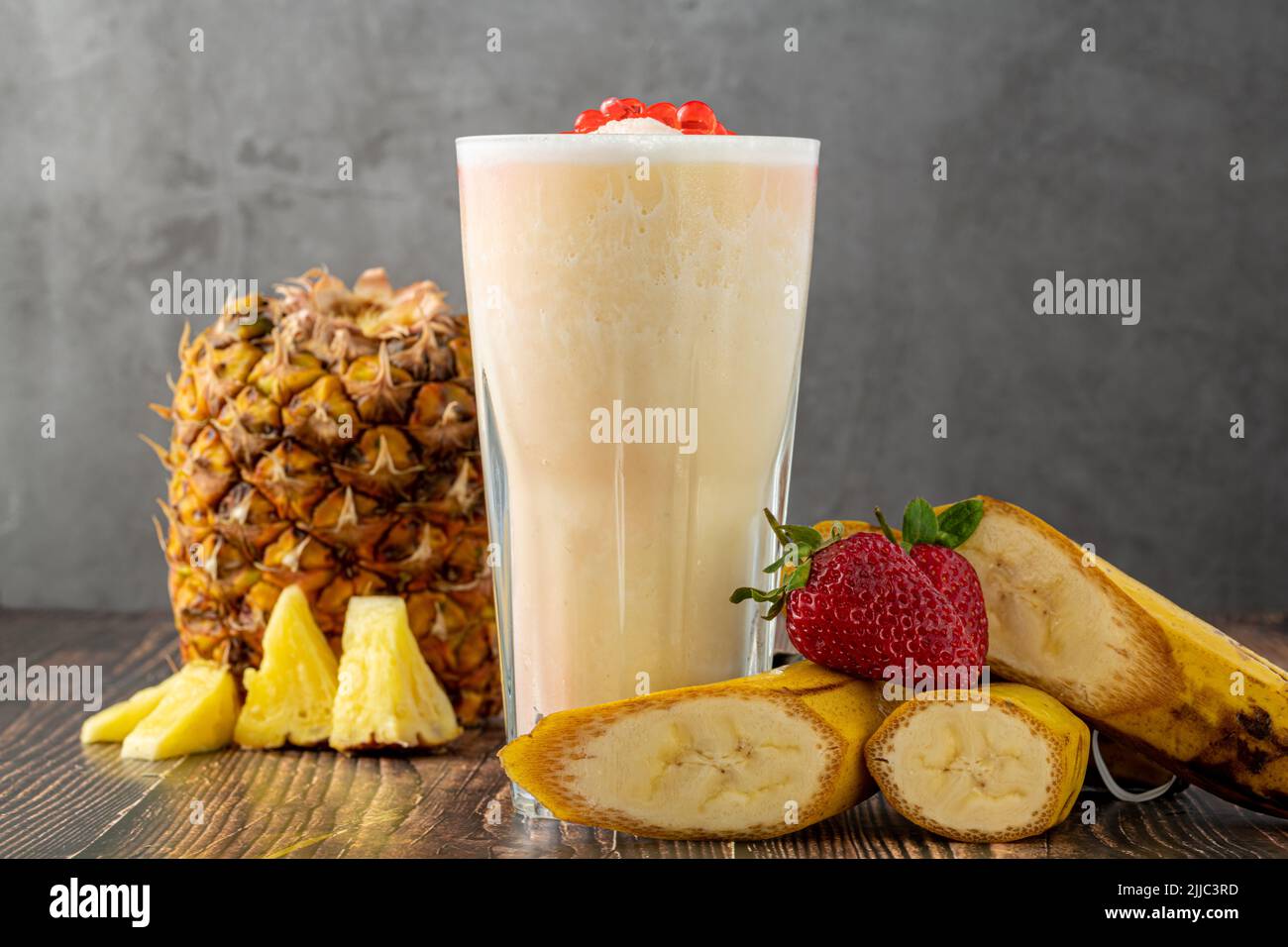Banana, strawberry and pineapple smoothie on wooden table and bubble tea or boba tea balls on it Stock Photo