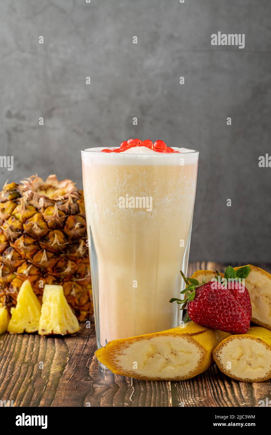Banana, strawberry and pineapple smoothie on wooden table and bubble tea or boba tea balls on it Stock Photo