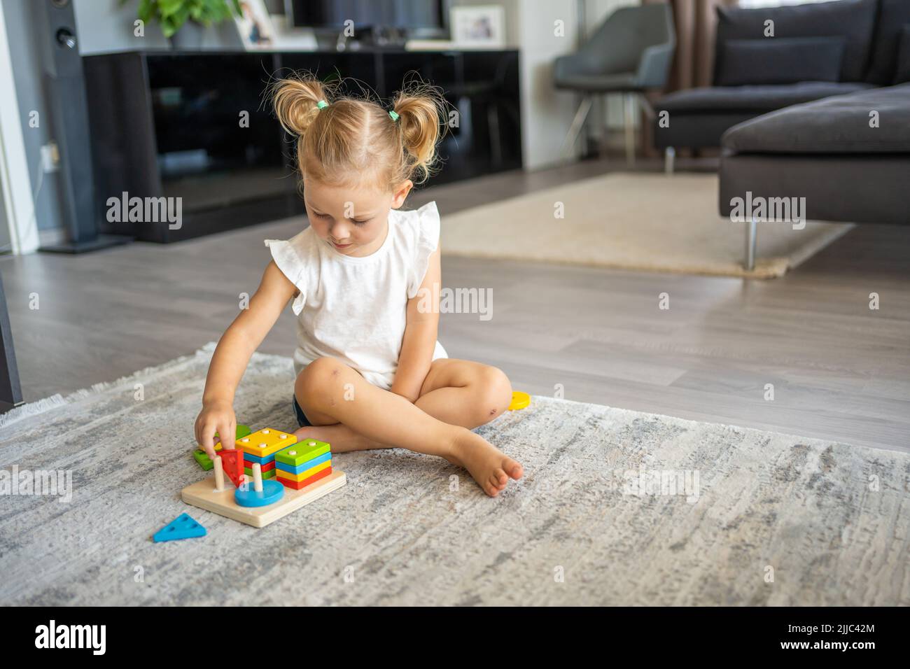 Cute caucasian little girl playing on the floor at home with eco wooden