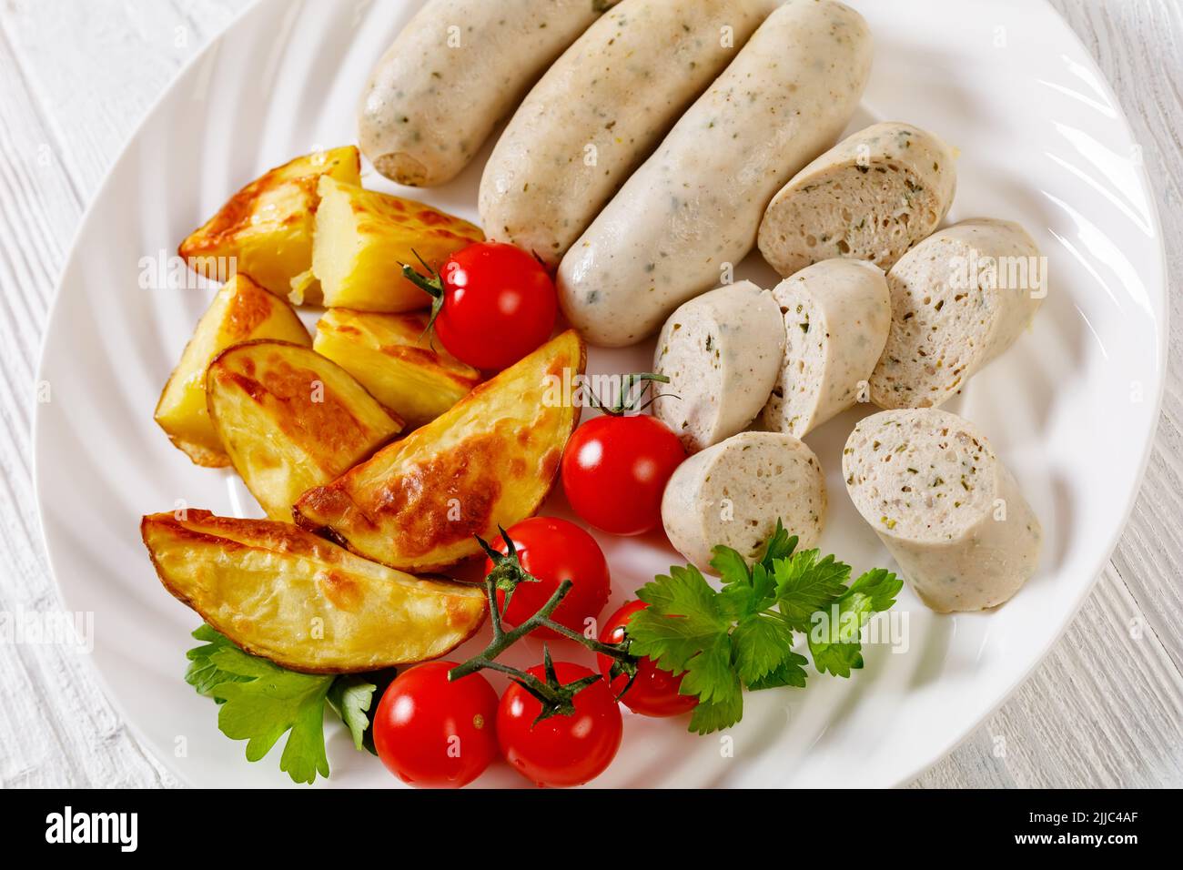 Weisswurst, bavarian white sausage of minced veal, pork back bacon, spices and parsley on white plate with roast potato, fresh tomatoes, horizontal vi Stock Photo