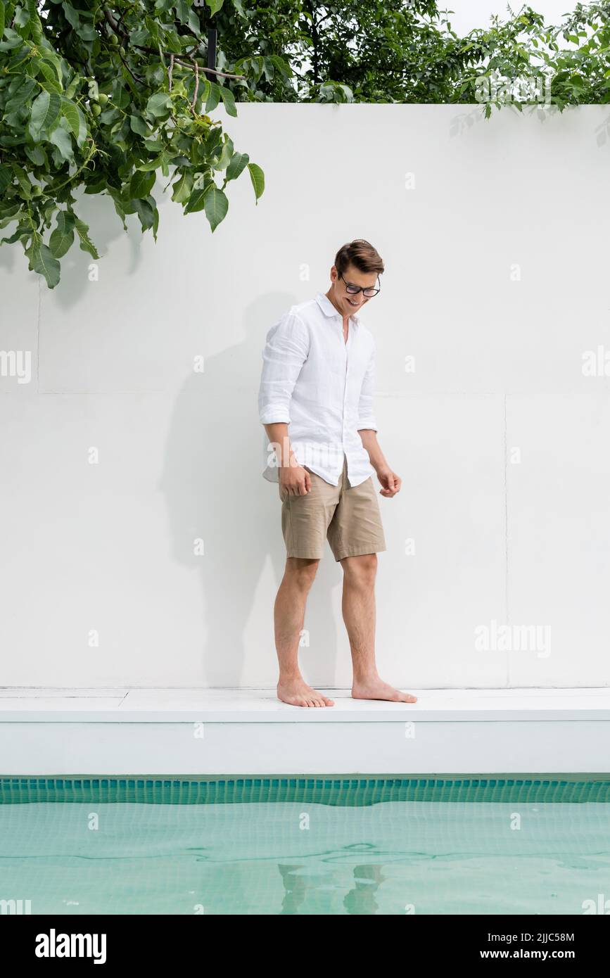 full length of barefoot man in shirt standing over pool near white wall ...