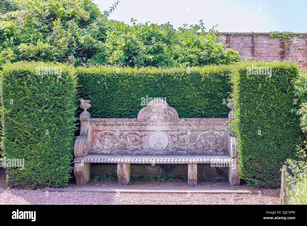 Stone carved vintage garden bench with decorations of acanthus leaves and scrolls in secluded corner of Tatton Park, UK. Stock Photo