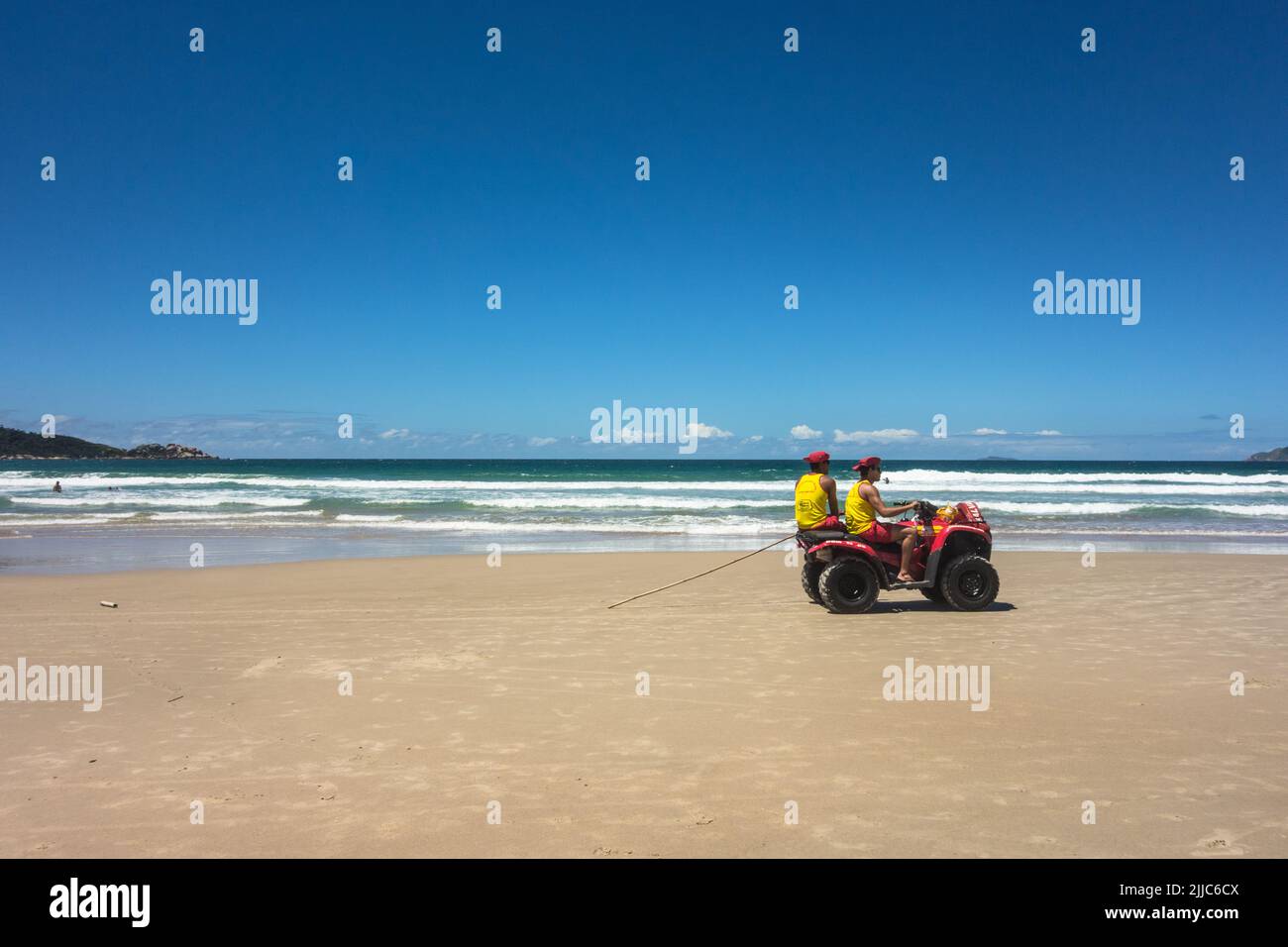 Red Quadricycle with two males lifeguards wearing a yellow t-shirt and  red hut driving on the beach with blue sky and calm sea Stock Photo