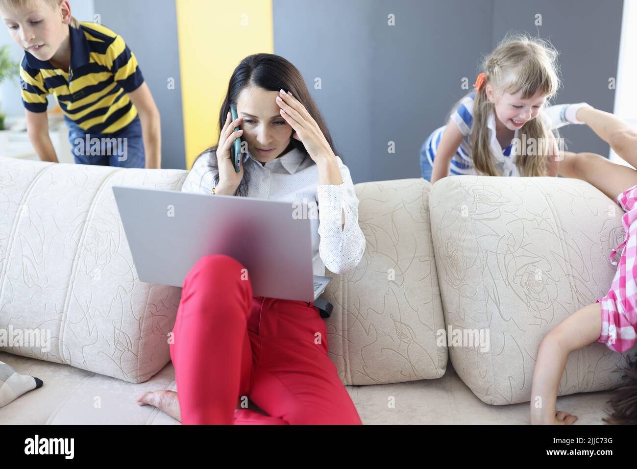 Woman working on laptop at home talking on phone and children playing Stock Photo