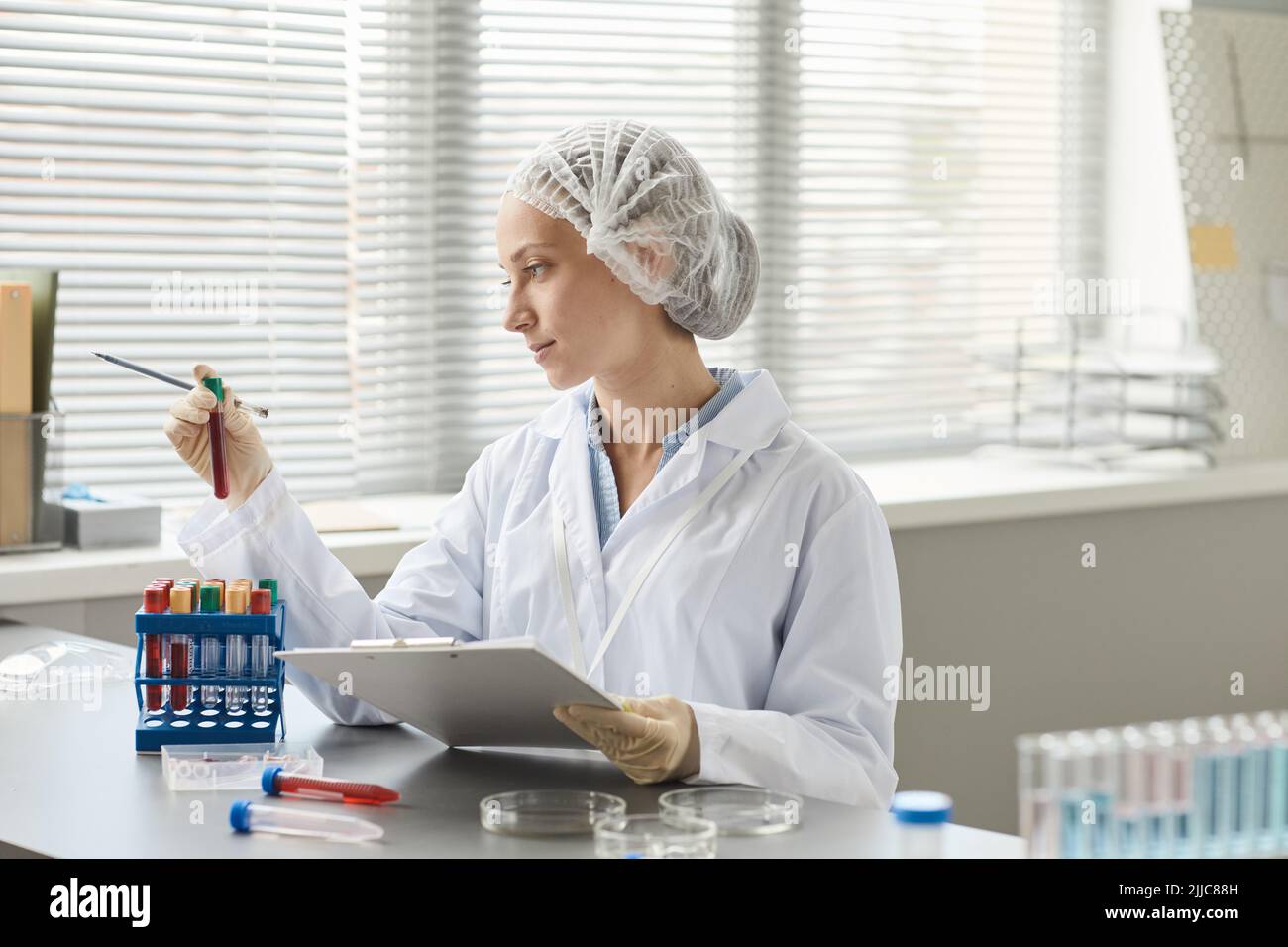 Side view portrait of young medical technician holding test tubes with blood samples in laboratory, copy space Stock Photo