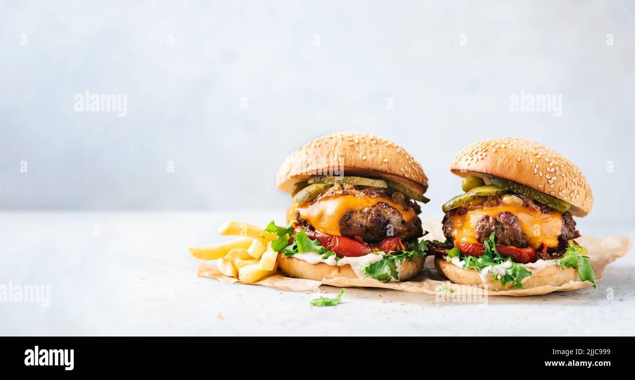 Two craft cheeseburgers and fries on parchment paper over grey concrete background. Copy space. Web banner burgers Stock Photo