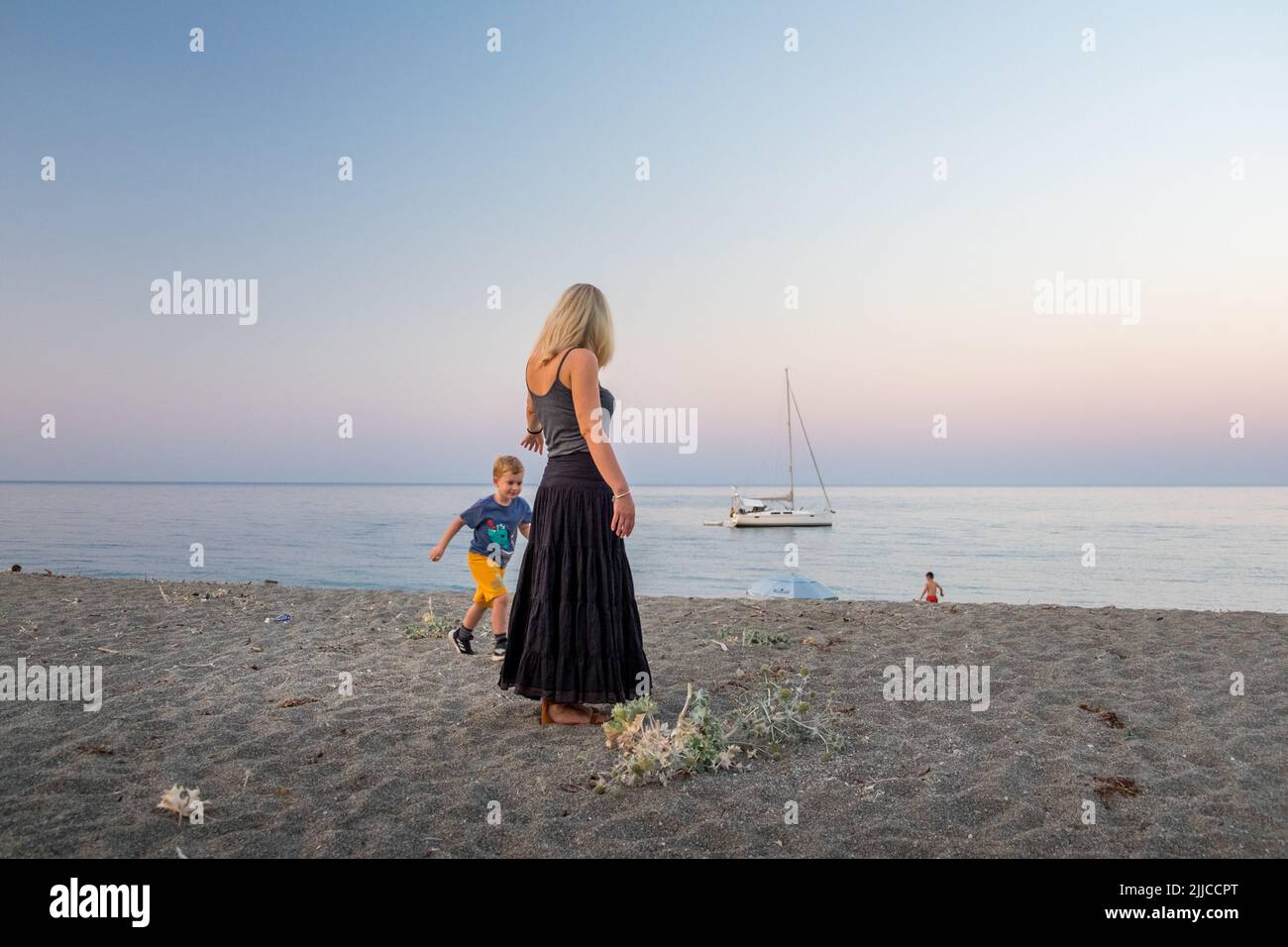 Little boy and his mother staring the sea and the sailboat at sunset time Agiokampos beach , Greece Stock Photo