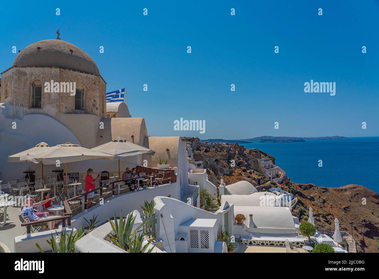 OIA, GREECE - MAY 22.2022: A church at Oia on Santorini island, Greece, people sitting in a restaurant Stock Photo