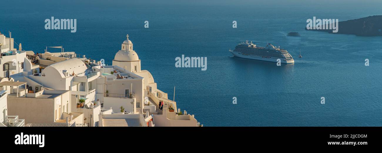 FIRA, GREECE - MAY 21.2022: View to the houses of Fira with a church, background a cruise ship, sea and Volcano of Santorini island, panorama Stock Photo
