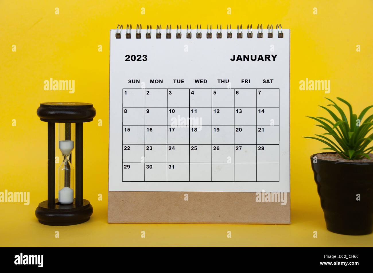 January 2023 desk calendar with table plant and minutes glass on yellow background. Calendar concept Stock Photo