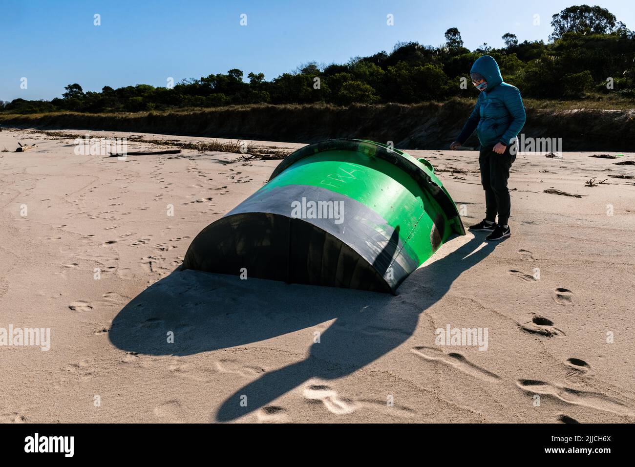 Woman standing next to a green signaling beacon that ran aground on the beach, Kiyu, San José, Uruguay Stock Photo