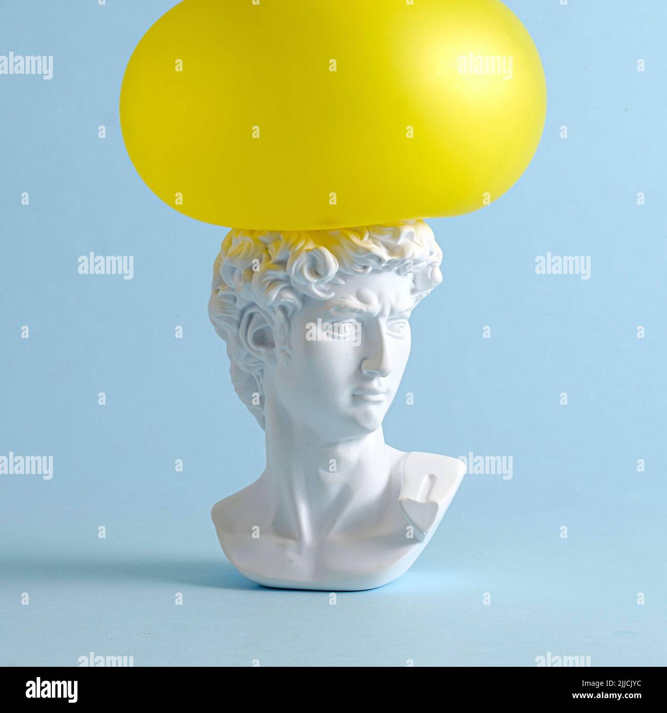 A yellow balloon presses on the head of David of an antique renaissance statue on a pastel blue background as a concept of pressure and problems. Stock Photo