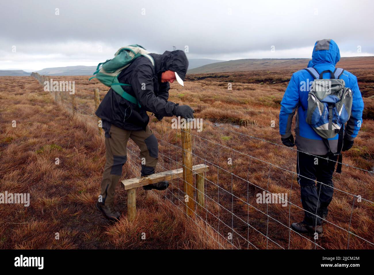 Two Men Climbing Wooden Stile in Wire Fence to the Summit of 'Horse Head' near Halton Gill in Littondale, Yorkshire Dales National Park, England, UK. Stock Photo