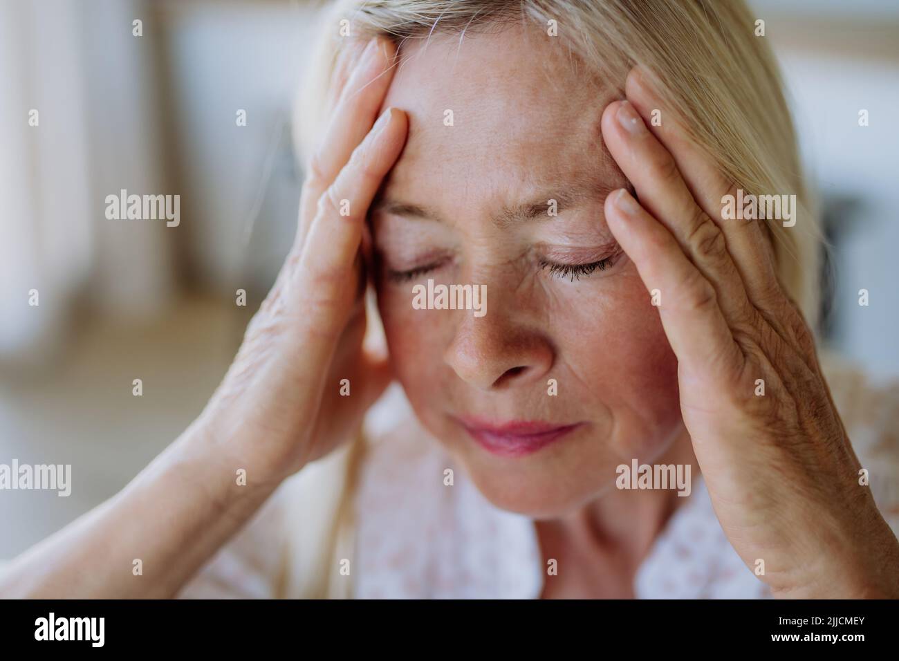 Portrait of an attractive senior woman sitting on a sofa at home with a headache Stock Photo