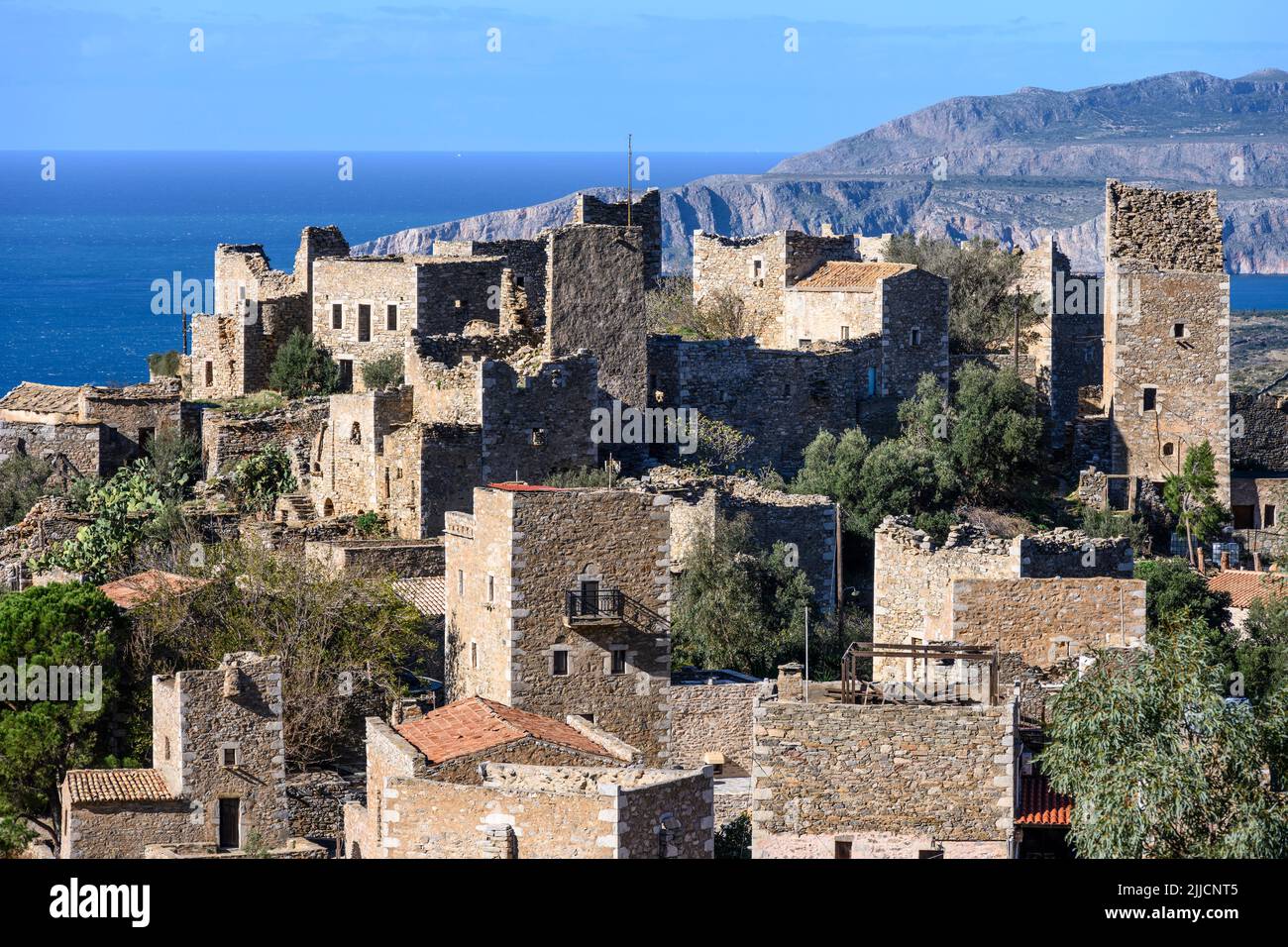 The stone towers and ruined houses of Vathia with the dramatic coast of the Deep Mani in the background, Southern peloponnese, Greece. Stock Photo